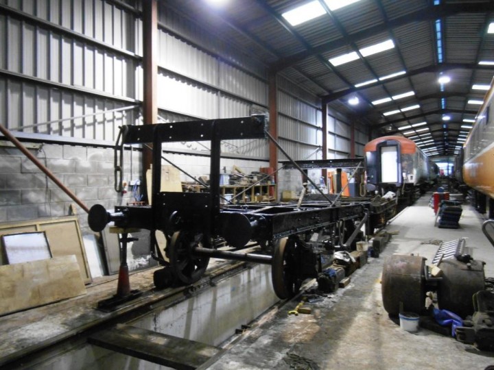 8/11/2016: The frames have been shunted over the pit in Carriage Shed A-Road and cleaning and painting is virtually finished. The wooden cradle has been removed and pieces can be seen beside the frames. Some can be re-used, most were too far gone and will be re-made by HEI. The corners at the Belfast end are being alternately jacked up to permit bearing insertion; this has raised the height of the frames nearest the camera by around 4 inches back to where they should be and the slope to Larne can clearly be seen, the wagon's buffers at that end being only level with the spare Mk2 Bogie behind them. (M.Walsh)
